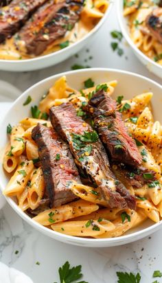 three white bowls filled with pasta and steak on top of a marble table next to utensils