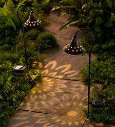 some lights that are on the side of a path near grass and trees in the evening