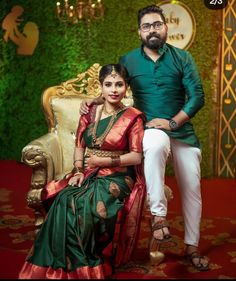 a man and woman posing for a photo in front of a green wall with greenery