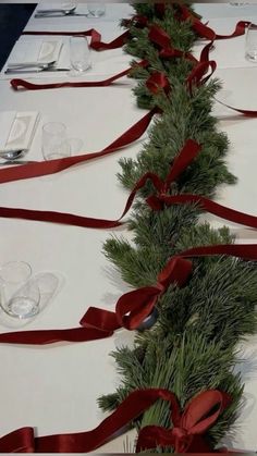 the table is decorated with red ribbon and greenery as well as empty wine glasses