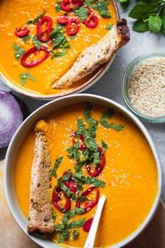 two bowls filled with soup and garnished with red peppers, parsley and bread