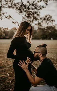 a pregnant couple kissing while sitting under a tree