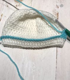 a crocheted white hat with blue trim on a wooden table next to scissors