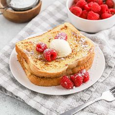 french toast topped with whipped cream and raspberries on a plate next to a bowl of strawberries