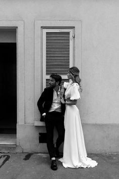 a man and woman standing next to each other in front of a building with shutters