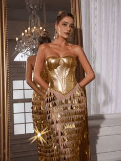 a woman in a gold dress standing next to a mirror with her hands on her hips