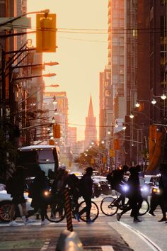 people crossing the street at an intersection with cars and bicycles in front of tall buildings