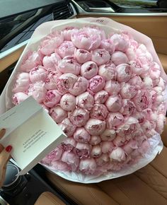 a bunch of pink flowers sitting on top of a car dashboard next to a note