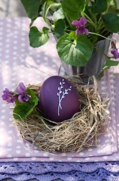 an egg sitting in a nest on top of a table next to some purple flowers