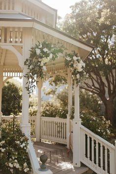 a gazebo with white flowers and greenery on the front porch for an outdoor wedding