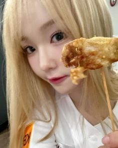 a girl with long blonde hair is holding a fried food item