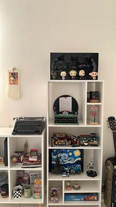 there is a book shelf with many books and toys on it in the corner next to an old typewriter