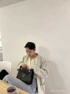 a woman sitting at a table with a black purse and cup of coffee in front of her