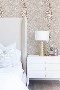 a white bed sitting in a bedroom next to a nightstand with a lamp on top of it