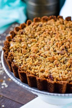 a pie sitting on top of a white cake plate covered in crumbled toppings