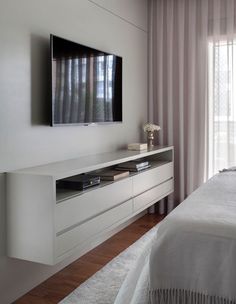 a flat screen tv mounted to the side of a white wall next to a bed