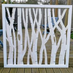 a white frame with trees cut out of it on top of a wooden deck next to blue chairs