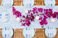 the table is set with plates, silverware and purple flowers on it's placemats