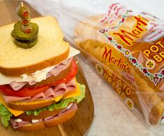 a sandwich with ham, lettuce and tomato on it next to a bag of potato chips