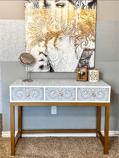 a white and gold painted dresser in front of a wall with a painting on it