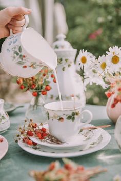 a person pours tea into a cup and saucer on a table with daisies