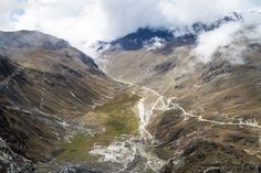 an aerial view of a mountain valley with clouds in the sky and mountains behind it