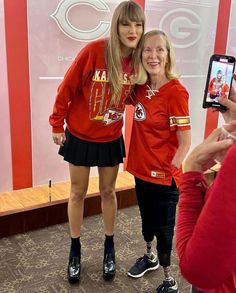 two women in red shirts taking pictures with their cell phones