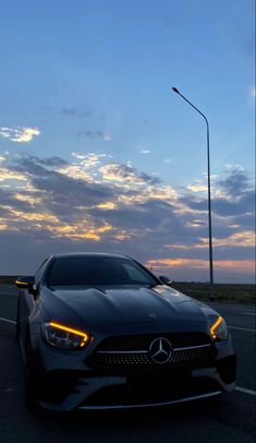 a black car driving down the road at dusk with clouds in the sky behind it