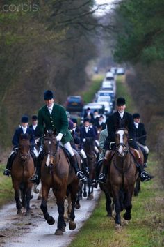 a group of people riding on the backs of brown horses down a road next to trees