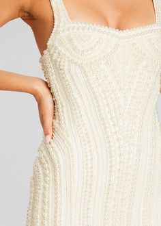 a woman wearing a white beaded dress with her hands on the back of her shoulder