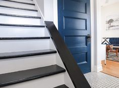 a blue door and some black steps in a white room with a rug on the floor