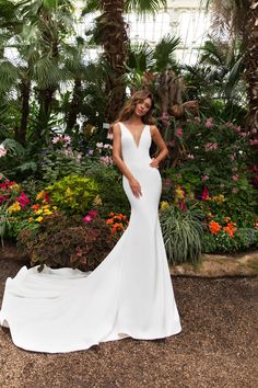 a woman in a white wedding dress standing next to flowers and palm trees with her hands on her hips