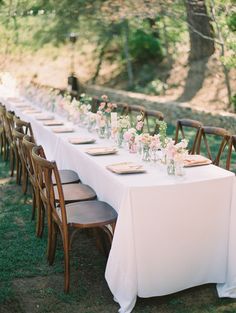 a long table is set up with flowers and place settings for an outdoor wedding reception