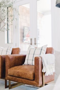 a brown leather chair sitting in front of a window next to a potted plant