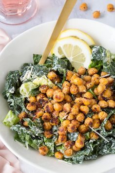 a white bowl filled with lettuce, chickpeas and lemon wedges