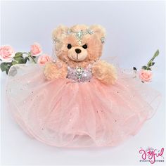 a teddy bear wearing a pink tutu with roses around it and a tiara on its head