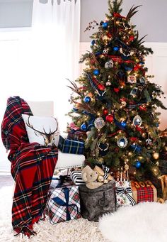 a christmas tree with presents under it in front of a plaid blanket and other holiday decorations