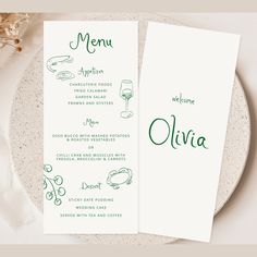 two menu cards with green ink on them sitting on a plate next to a glass of wine