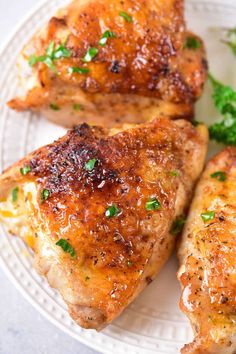 three pieces of chicken on a white plate with parsley sprinkled around it