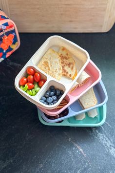 four plastic containers filled with food on top of a black table next to a wooden box