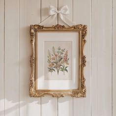 an ornate gold frame hangs on the wall above a floral print with a white bow