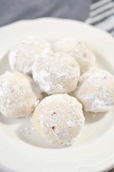 several powdered sugar donuts on a white plate with a striped napkin in the background