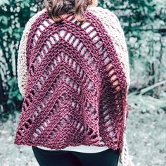 a woman wearing a red and white crocheted shawl in front of trees