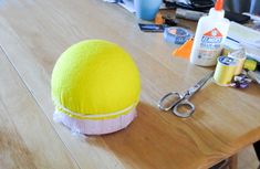 a large yellow ball sitting on top of a wooden table next to scissors and glue