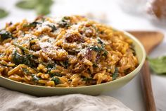 a bowl of pasta with spinach and parmesan cheese on top, next to a wooden spoon