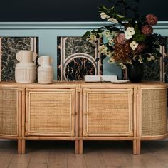 a sideboard with vases and flowers on it in front of a blue wall