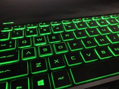 a close up view of a keyboard with green light on it's keys and backlight