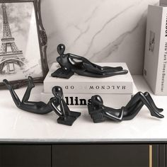 three small black figurines sitting on top of a white table next to a book