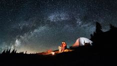 two people are sitting at a camp site under the night sky with their tent in the foreground