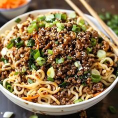 a white bowl filled with noodles, meat and veggies next to chopsticks